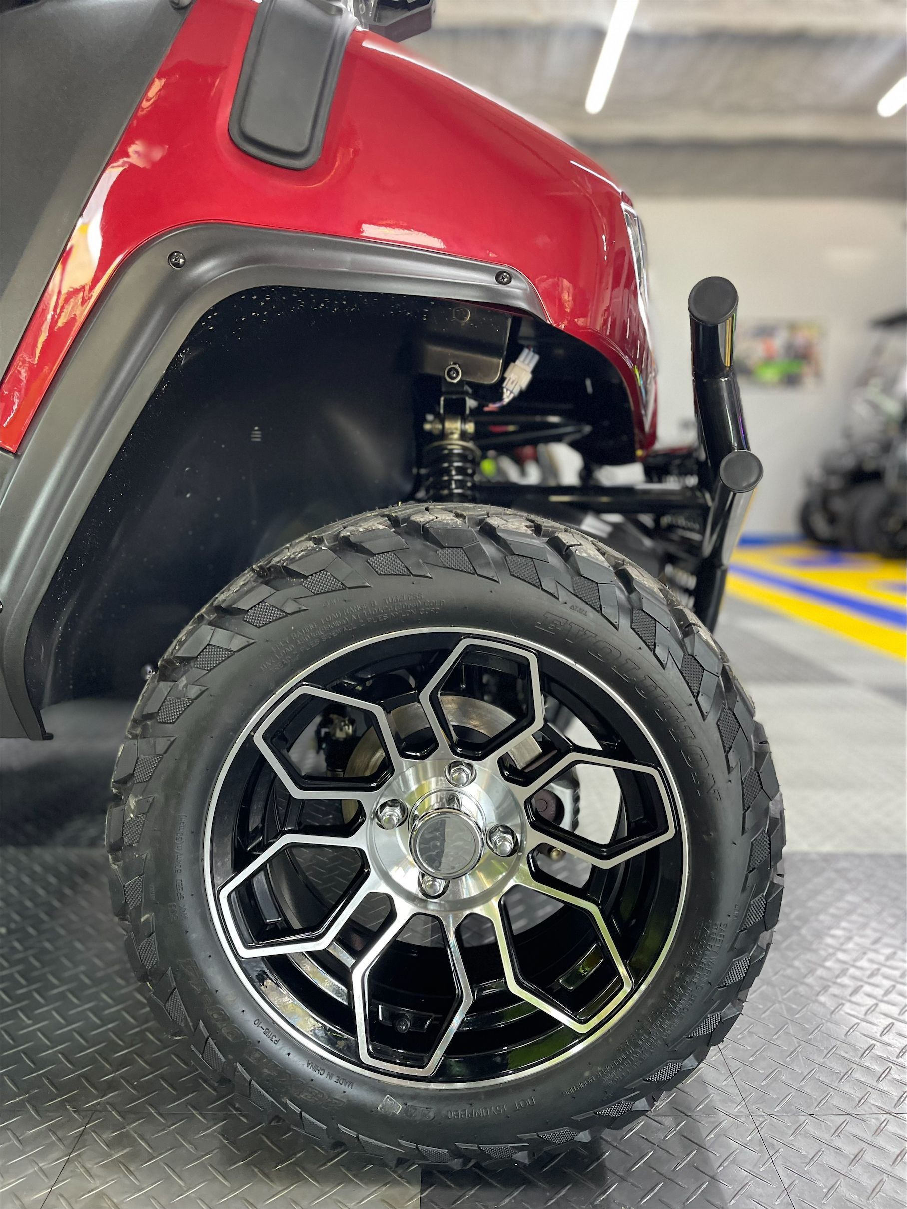 Close-up of a red golf cart's front wheel with black and silver rims and a rugged tire, showing suspension details.