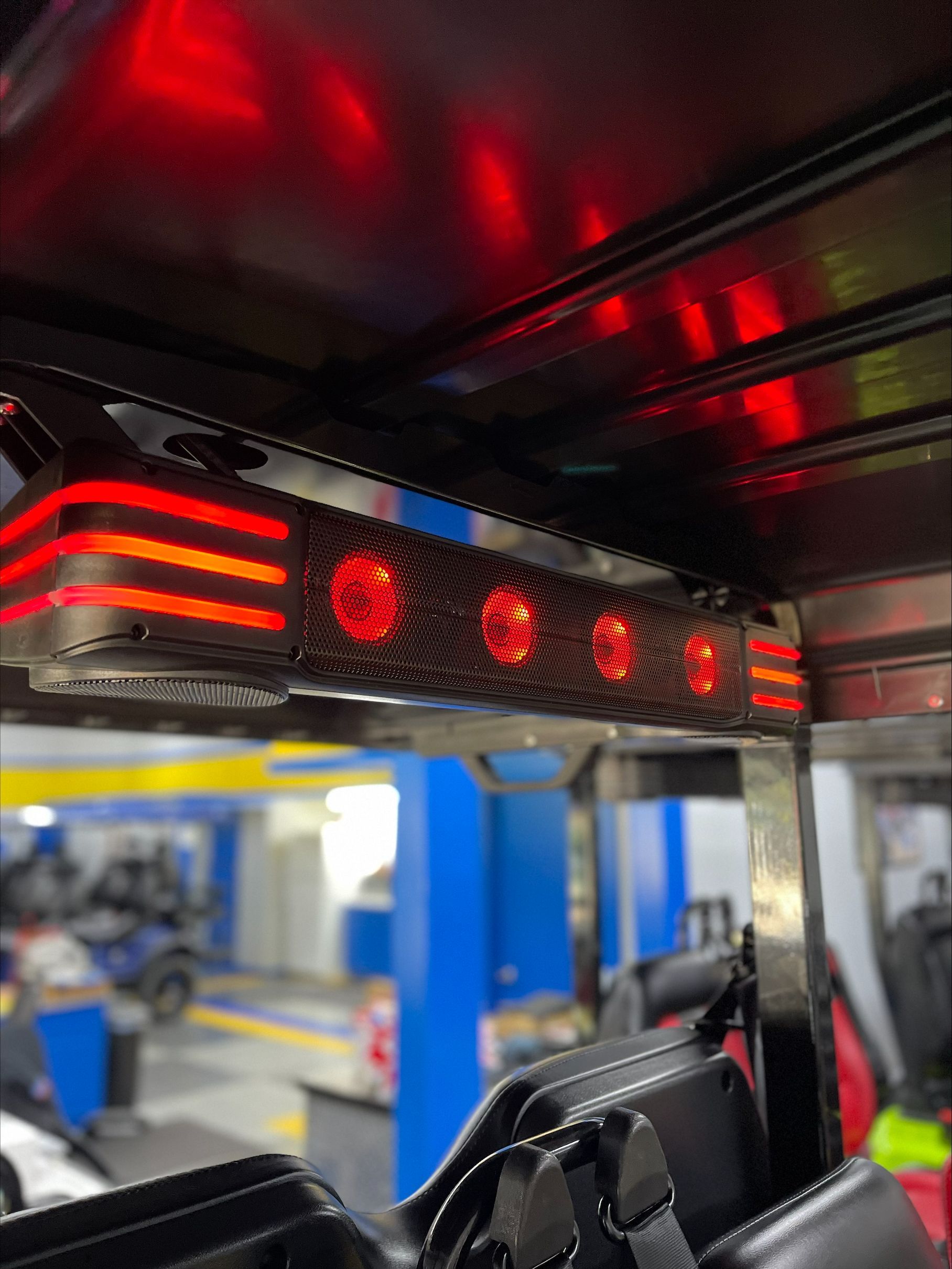 Red interior lights on a vehicle, possibly a tuk-tuk or similar small transport, with a blurry workshop background.