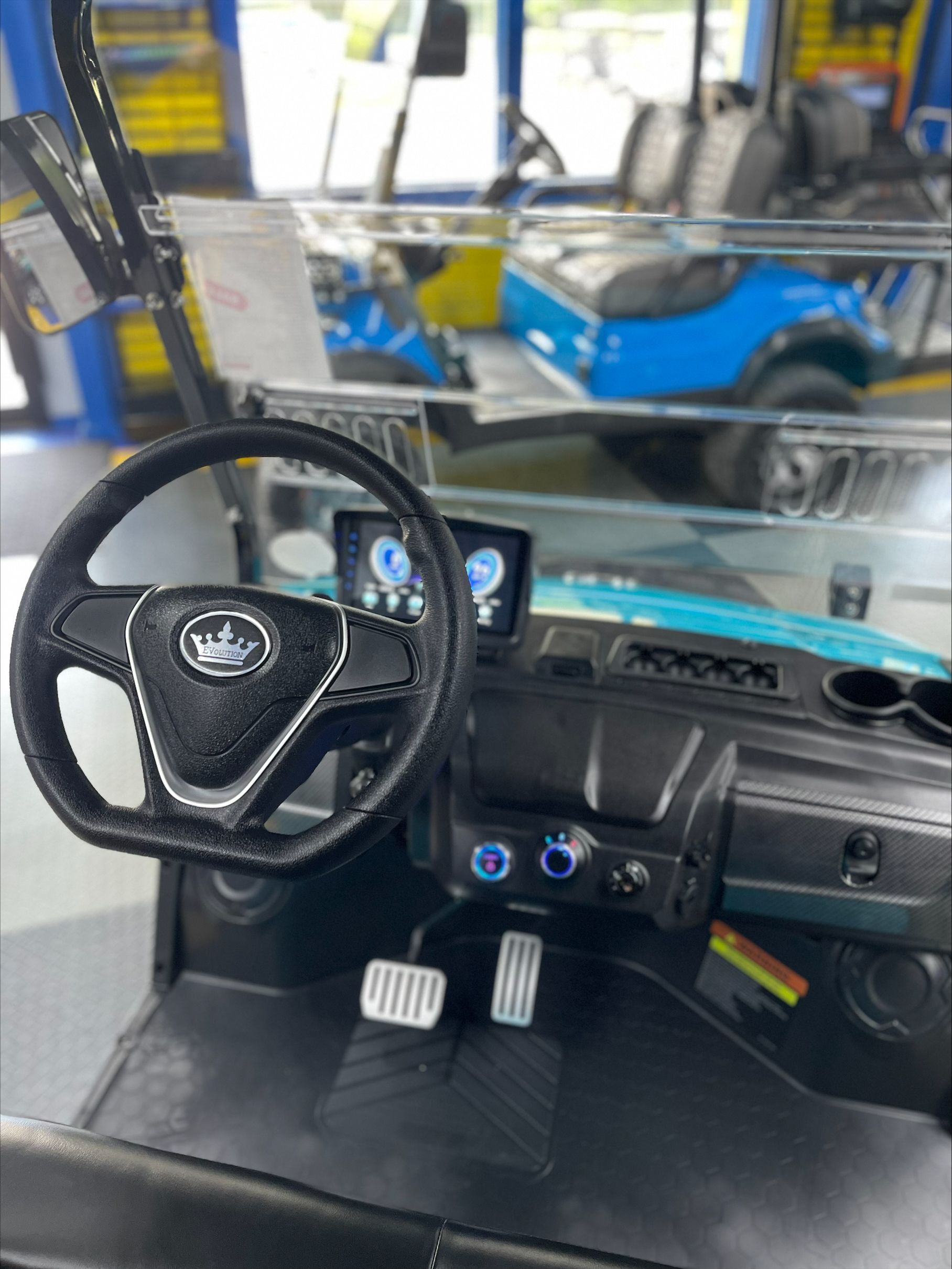 Interior view of a teal golf cart with a black steering wheel, digital display, and cup holders, likely in a showroom.