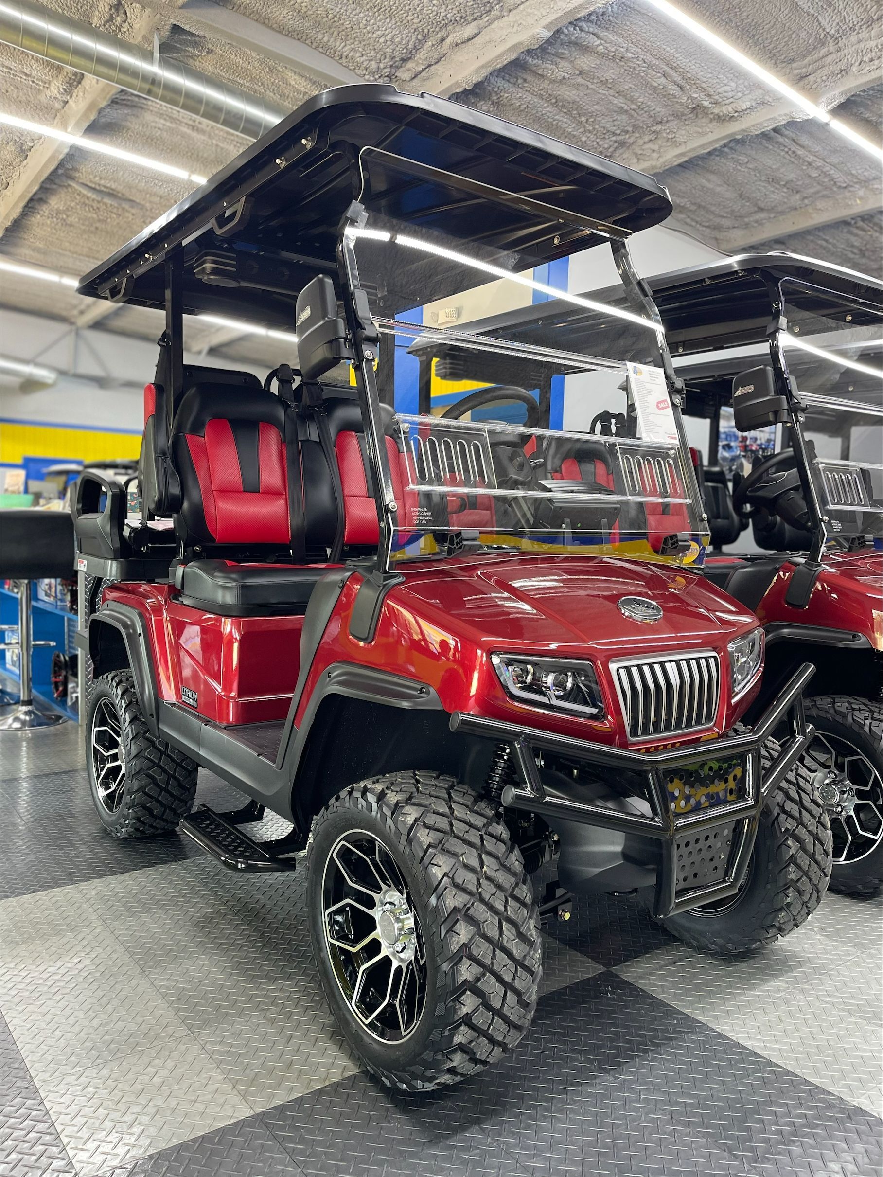 Red and black golf cart with off-road tires and a black roof, parked inside a building.