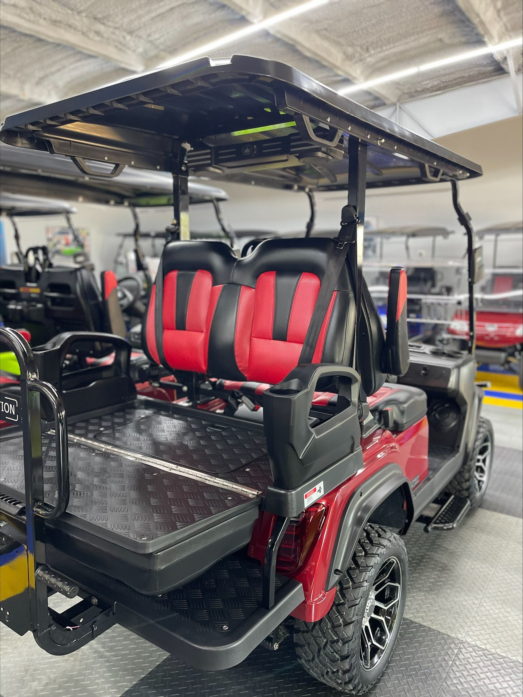 Red and black golf cart with a diamond plate cargo bed and black and red seating, inside a garage.