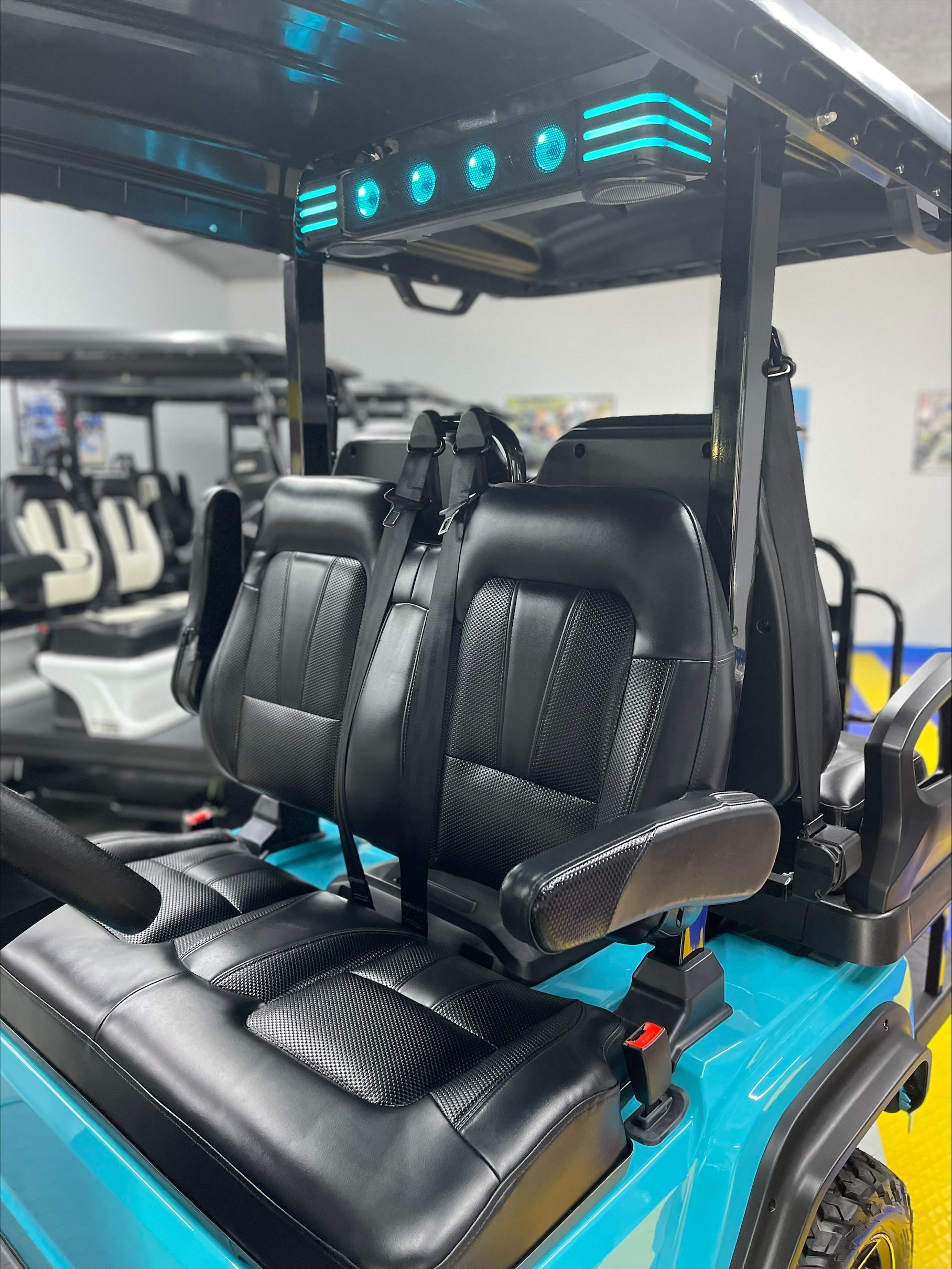 Teal golf cart interior with black quilted seats and blue overhead lighting.