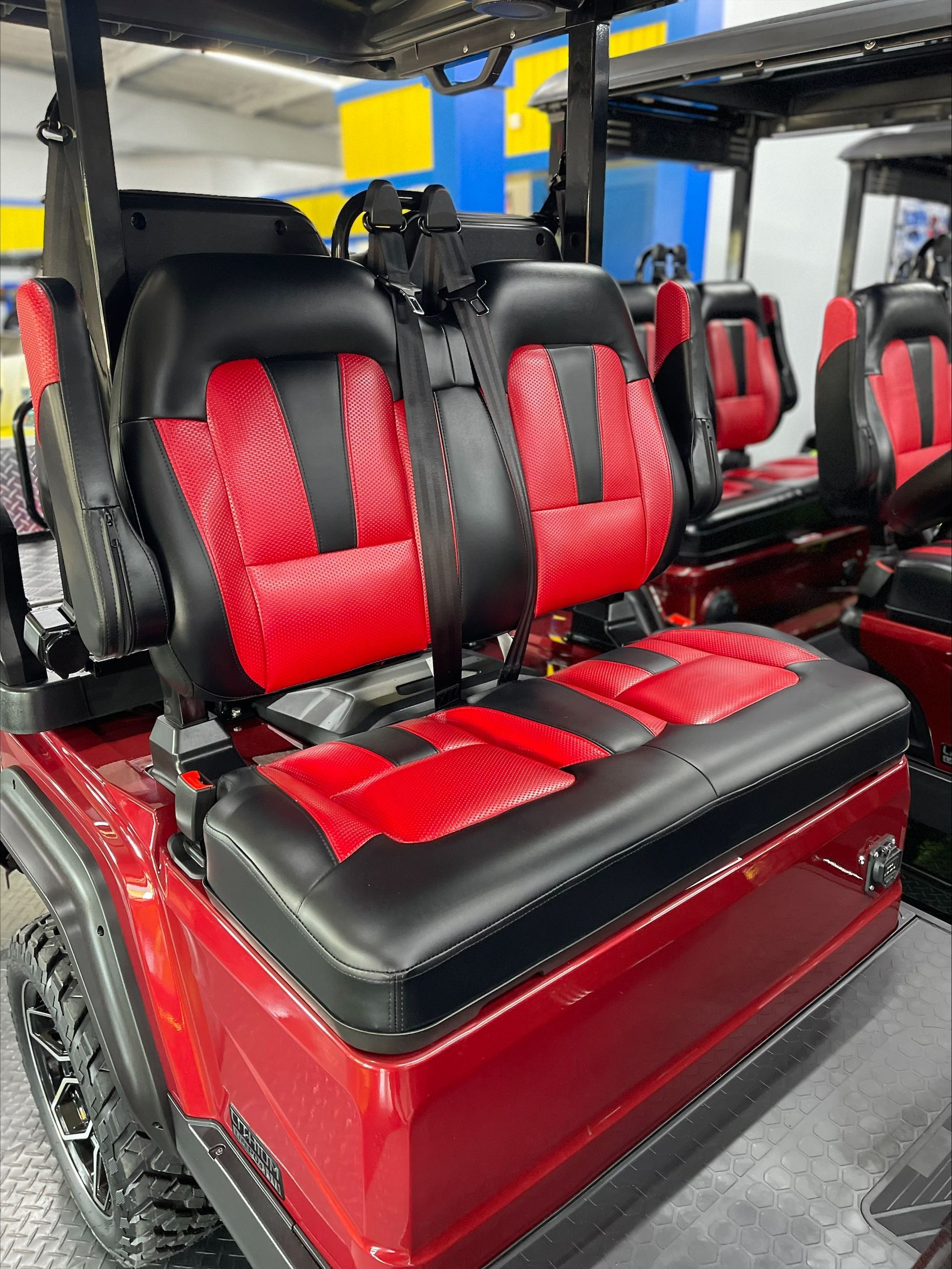 Red and black golf cart seats in a showroom. The seats are heavily cushioned with a two-tone design.