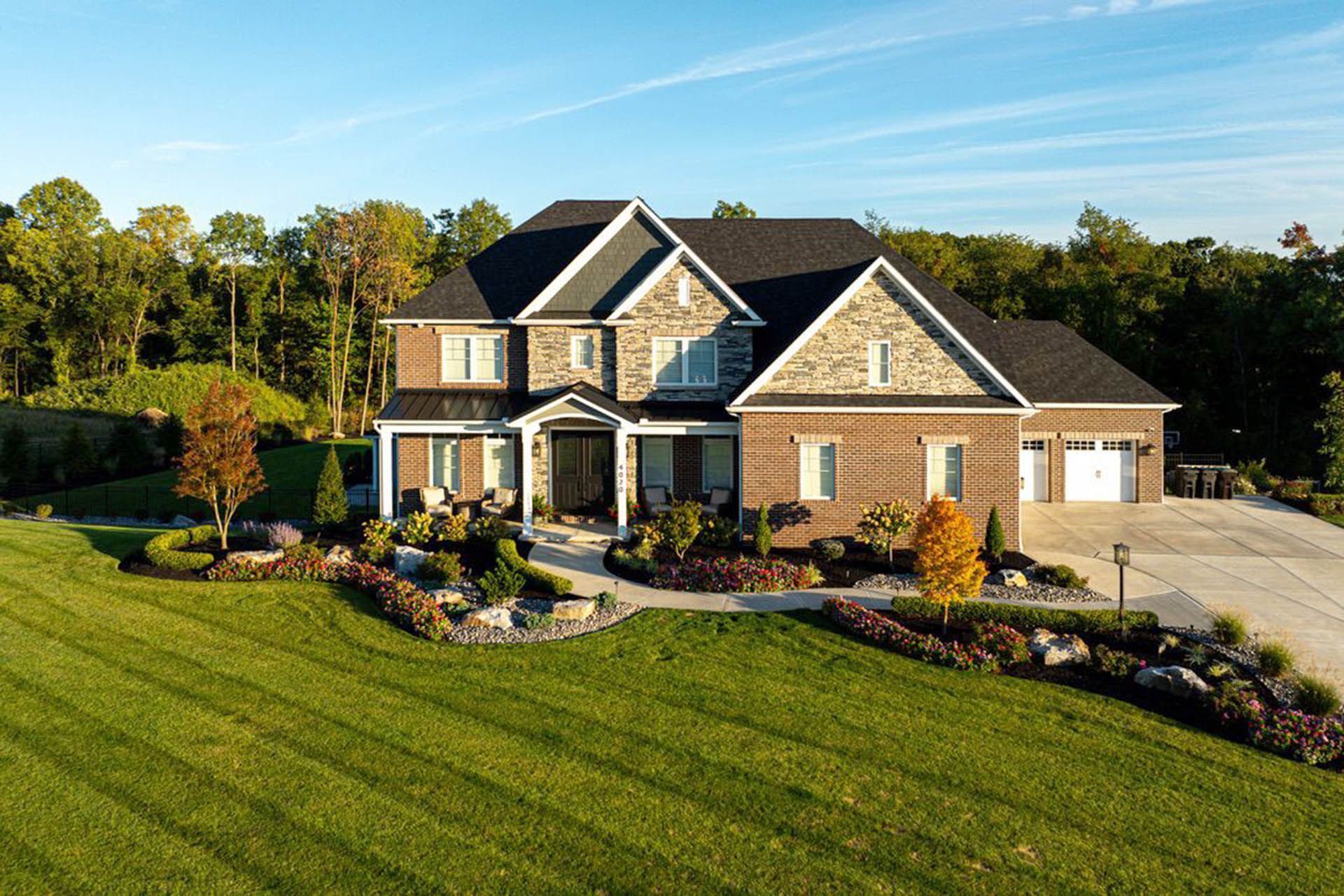 A huge house with brick and stone exterior, beautiful lawn, and landscaped flowerbeds