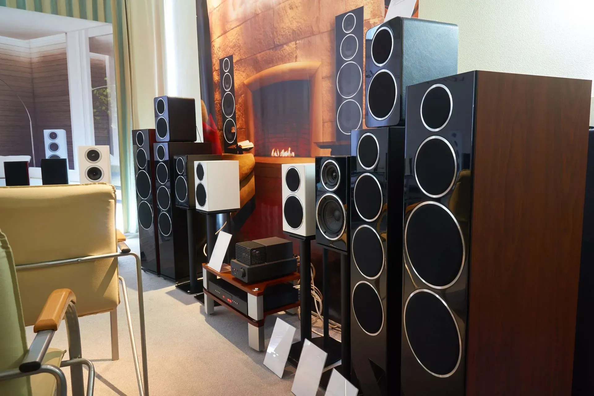 Array of black and white speakers on display in a room, with chairs and shelving visible.