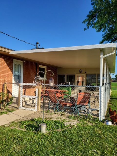 A covered porch with chairs and a table in front of a brick house.