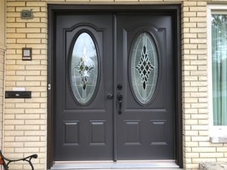A black double door with oval windows on a brick wall.