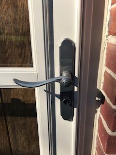 A close up of a door handle on a white door next to a brick wall.