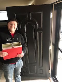 A man is holding a red box in front of a black door.