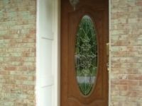 A wooden door with a stained glass window on a brick wall.