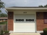 A white garage door is sitting in front of a brick house.