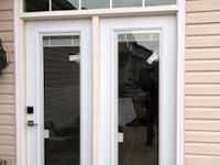 A white sliding glass door with a window above it on the side of a house.