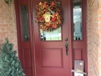 A red door with a wreath on it and a christmas tree in front of it.