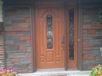 A wooden door with a glass window is on a brick wall.