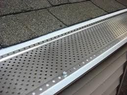 A gutter with holes in it is on the roof of a house.