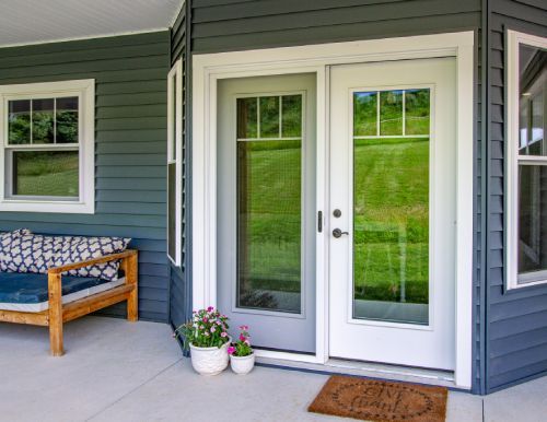 A porch with a couch and a door with a reflection of a field.