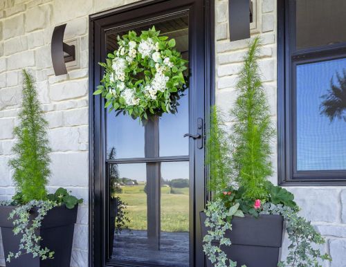 A black door with a wreath on it and potted plants in front of it.