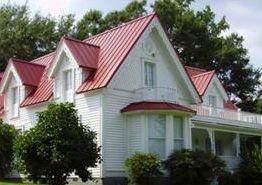 A white house with a red roof is surrounded by trees.