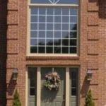 The front door of a brick house with a wreath on it and a large window.