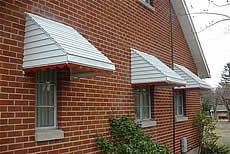 A red brick house with white awnings on the windows.