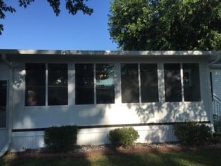 A white mobile home with a screened in porch and lots of windows.