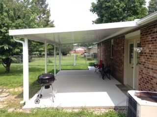 A covered patio with a grill and chairs underneath it.
