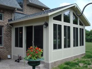A screened in porch with a brick house in the background.