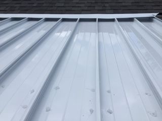 A close up of a white metal roof with a roof in the background.