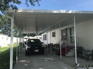 A car is parked under a canopy in front of a mobile home.