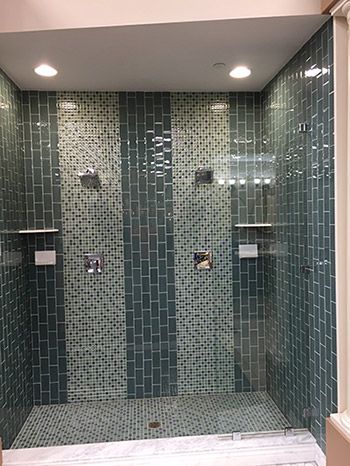A walk in shower with green tiles and a glass door.