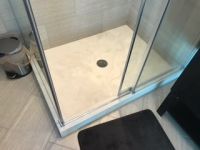 A shower stall in a bathroom with a black rug and a trash can.