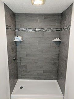 A shower stall with a gray tiled wall and a white shower base.