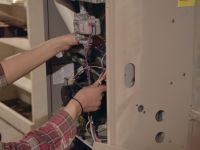 A person is working on a furnace with a screwdriver.