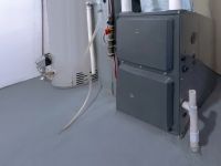 A gray furnace is sitting next to a water heater in a basement.