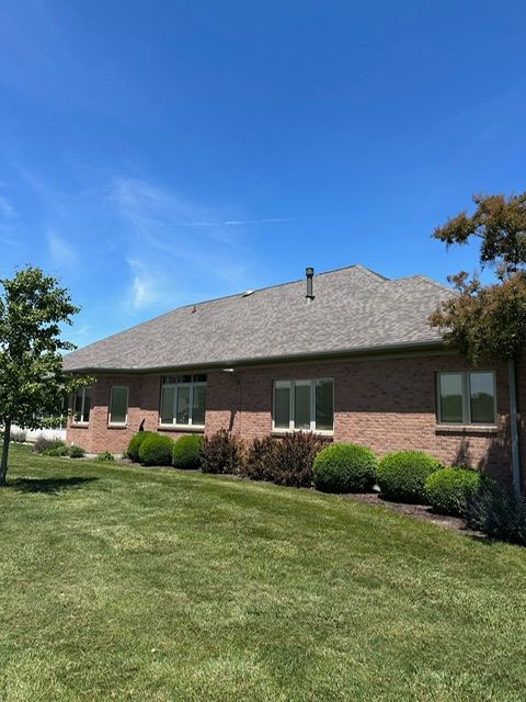 A brick house with a gray roof and a lush green lawn in front of it.