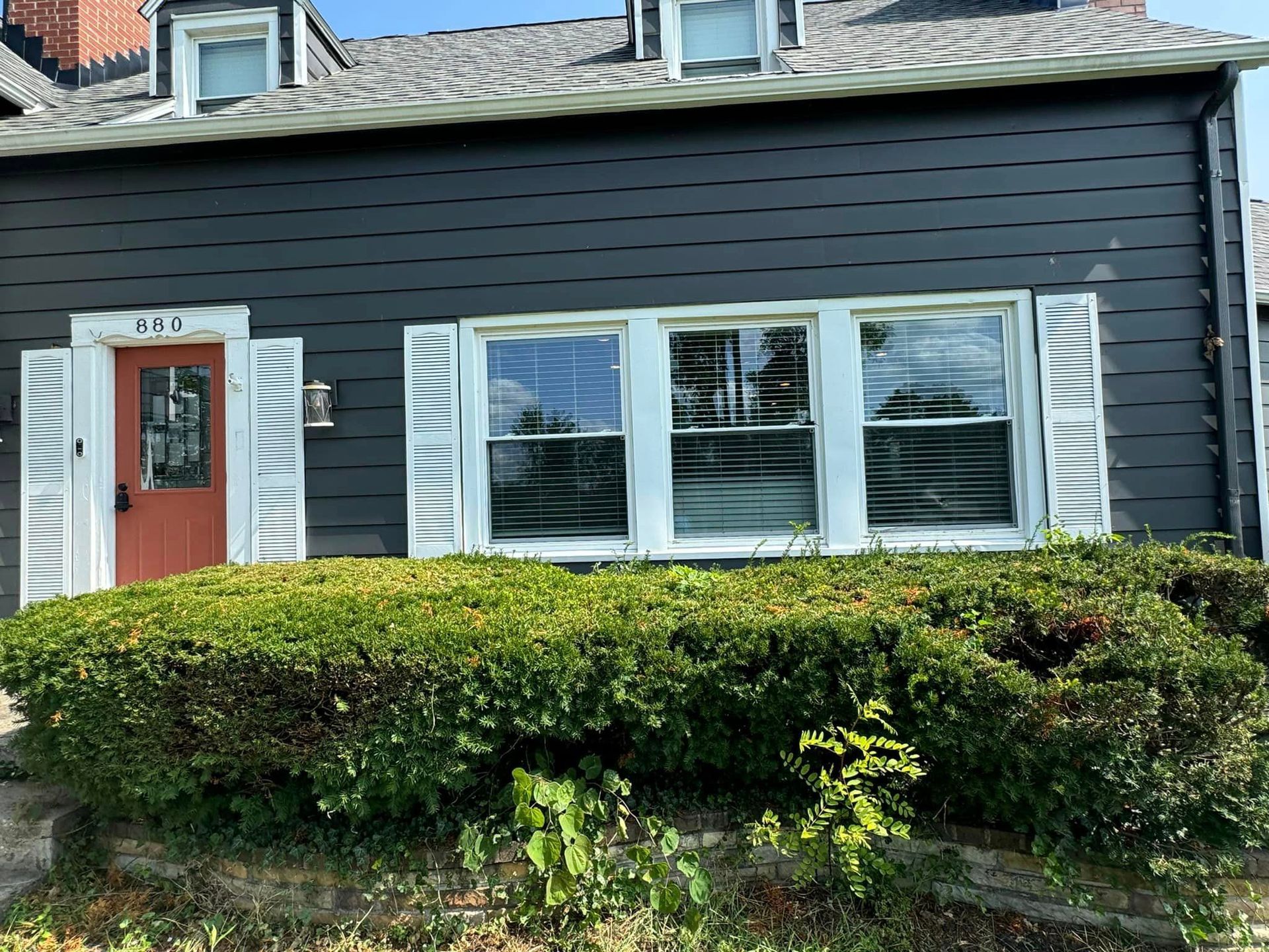 A black house with white shutters and a red door