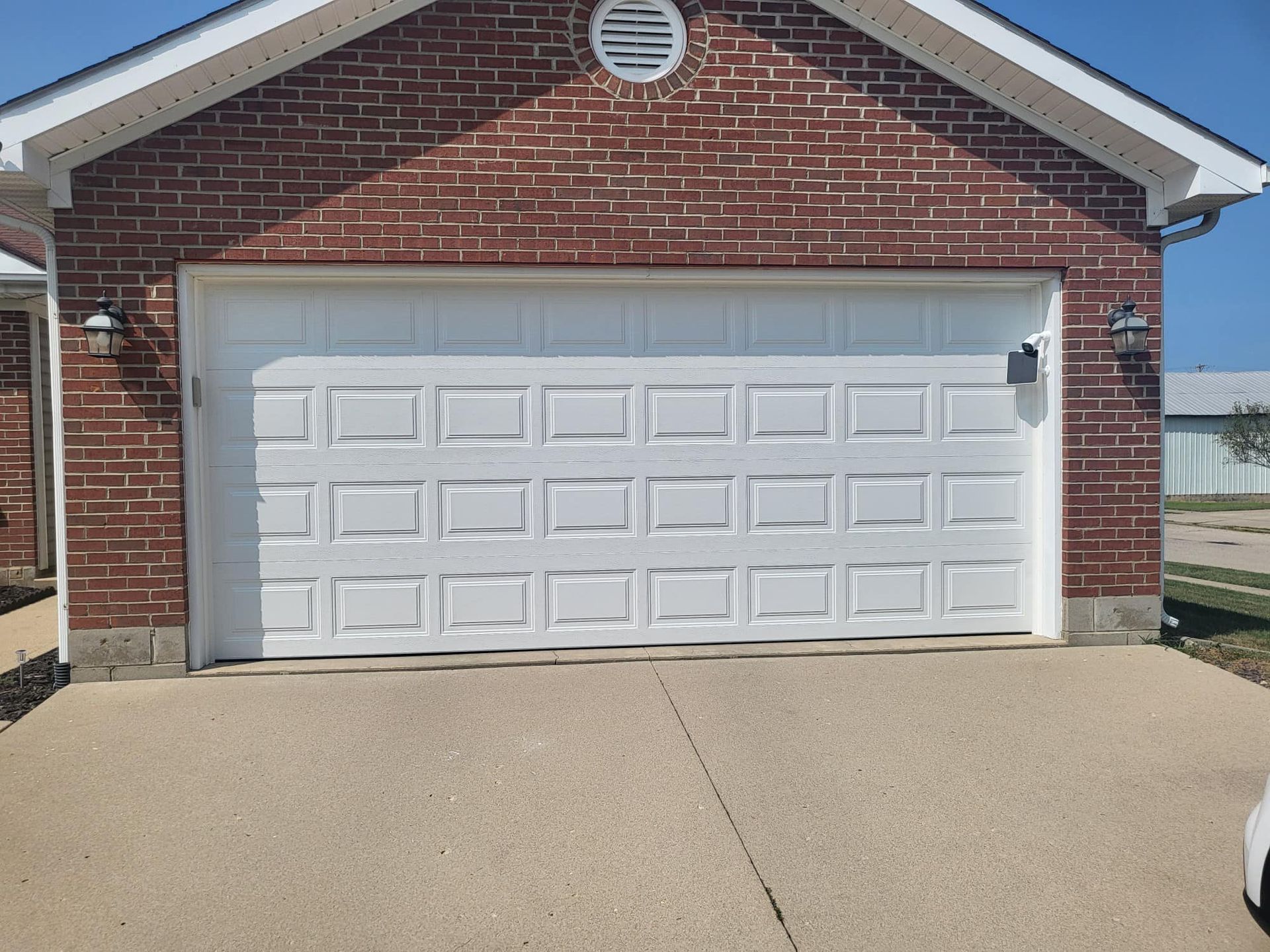 A white garage door is sitting in front of a brick house.
