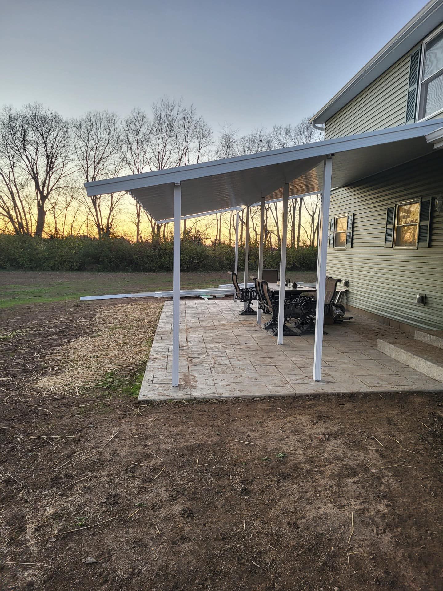 A covered patio with a table and chairs in front of a house.