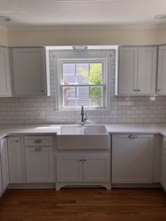 A kitchen with white cabinets , a sink , and a window.