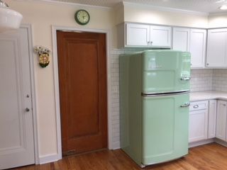A green refrigerator is sitting in a kitchen next to a door.