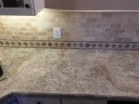 A kitchen with a marble counter top and a tile backsplash.