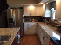 A kitchen with white cabinets , granite counter tops , stainless steel appliances and a refrigerator.