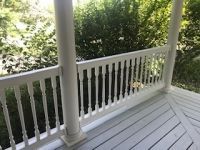 A porch with a white railing and trees in the background.