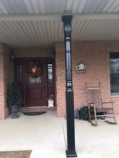 There is a rocking chair on the porch of a brick house.