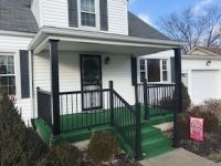 A white house with a green porch and black railing.