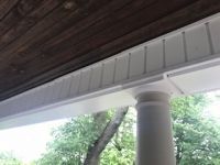 A porch with a white siding and a wooden ceiling.