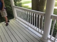 A man is standing on a porch with a white railing.