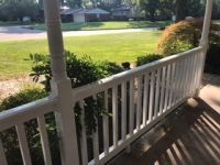 A porch with a white railing and a view of a lush green field.