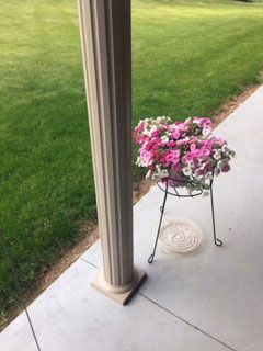 A potted plant with pink and white flowers on a stand on a porch.