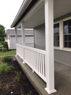 A porch with a white railing and a gray house in the background.